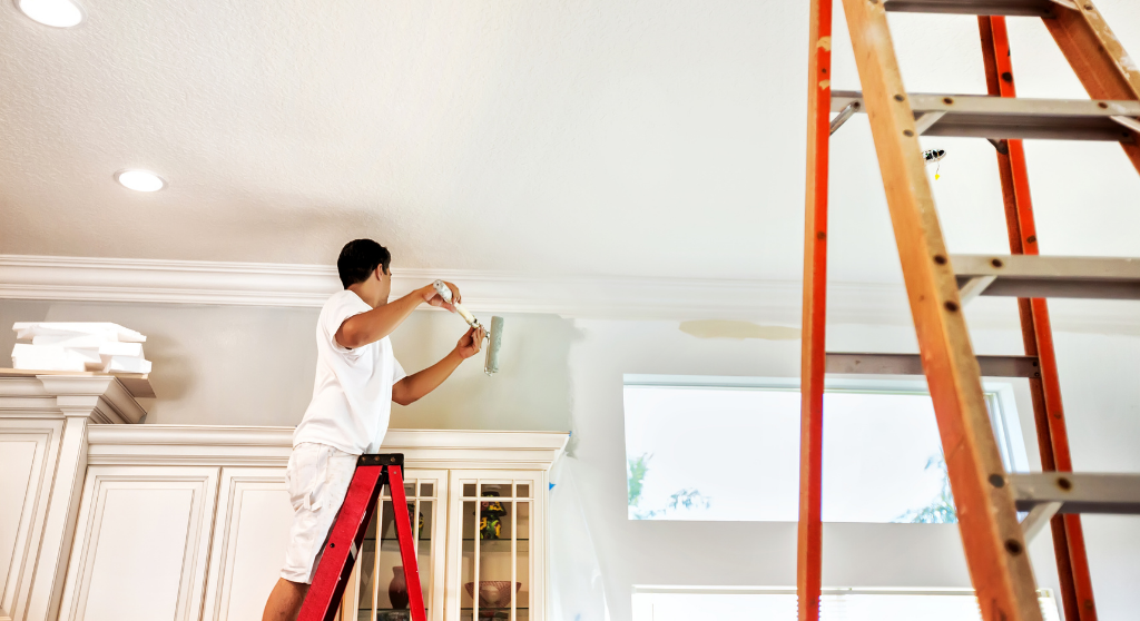 Man on a ladder painting the wall